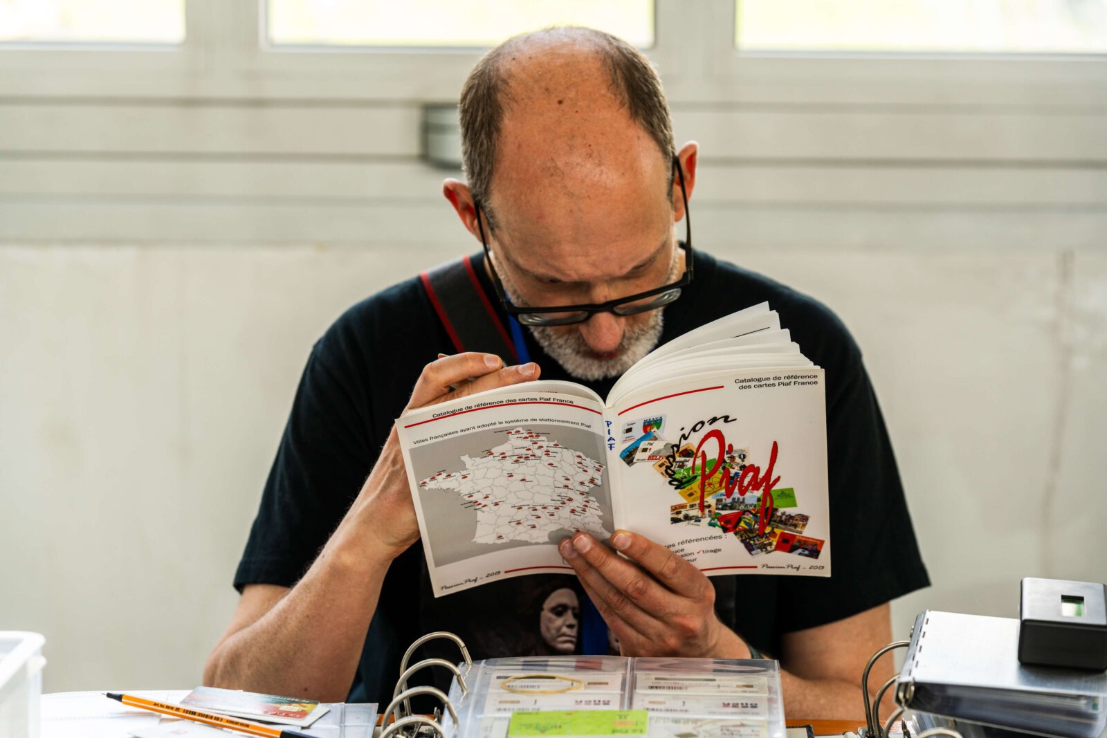Collector studying a phonecard reference catalog at PIM 2026, the research behind the Contribute to History project