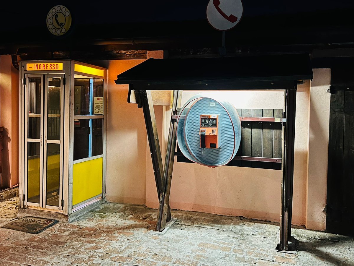 Illuminated telephone booth and payphone display at Museo Telefonia Pubblica at night
