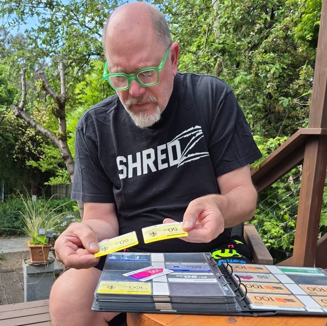 Eric Schuenemann holding two vintage Tamura and Anritsu phonecards from Venezuela, with his open phonecard album on his lap
